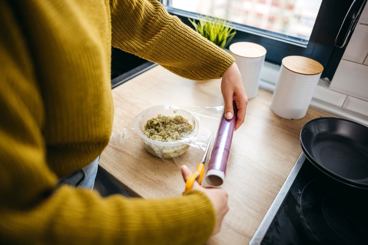 Young woman protecting food in kitchen with foil