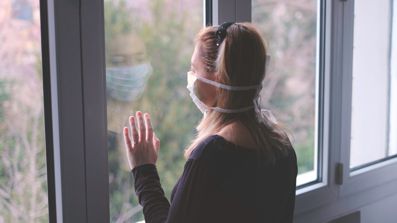 a white woman wearing a face mask stares out the window