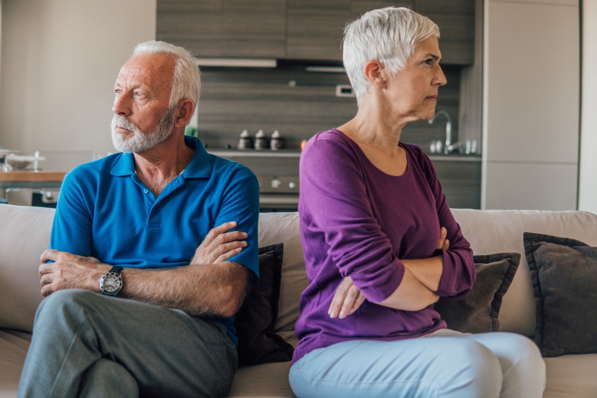 Senior married couple having an argument as they look away from each other with arms folded on couch