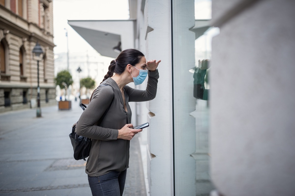 Woman wearing protective mask, using mobile phone. She is outdoors, in a street. Belgrade, Serbia