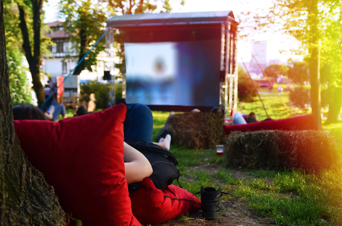 Person laying on red pillows on green Grass looking on big Screen