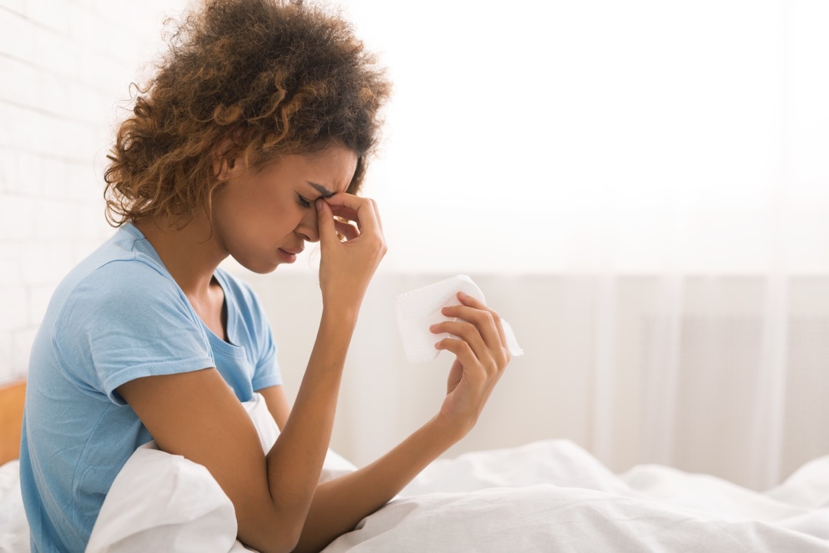 Young sick woman with flu blowing her nose, sitting in bed