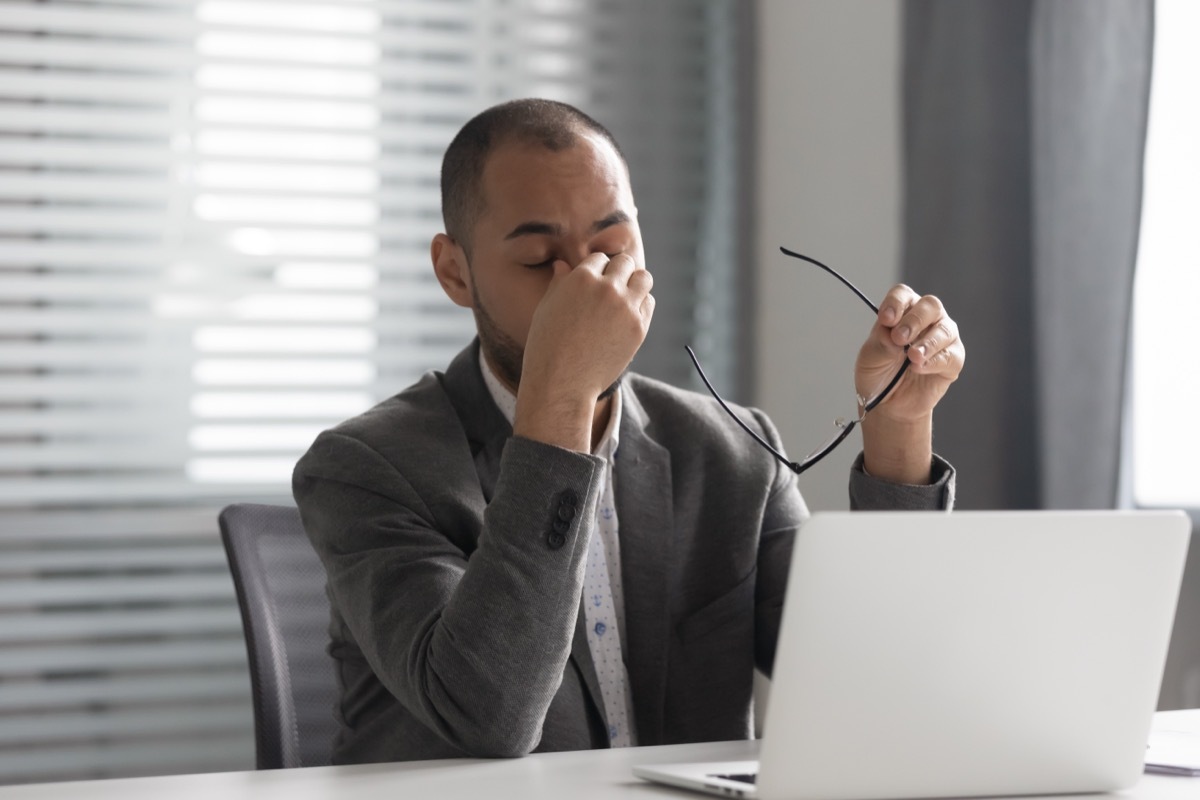 man sitting at laptop rubbing eyes