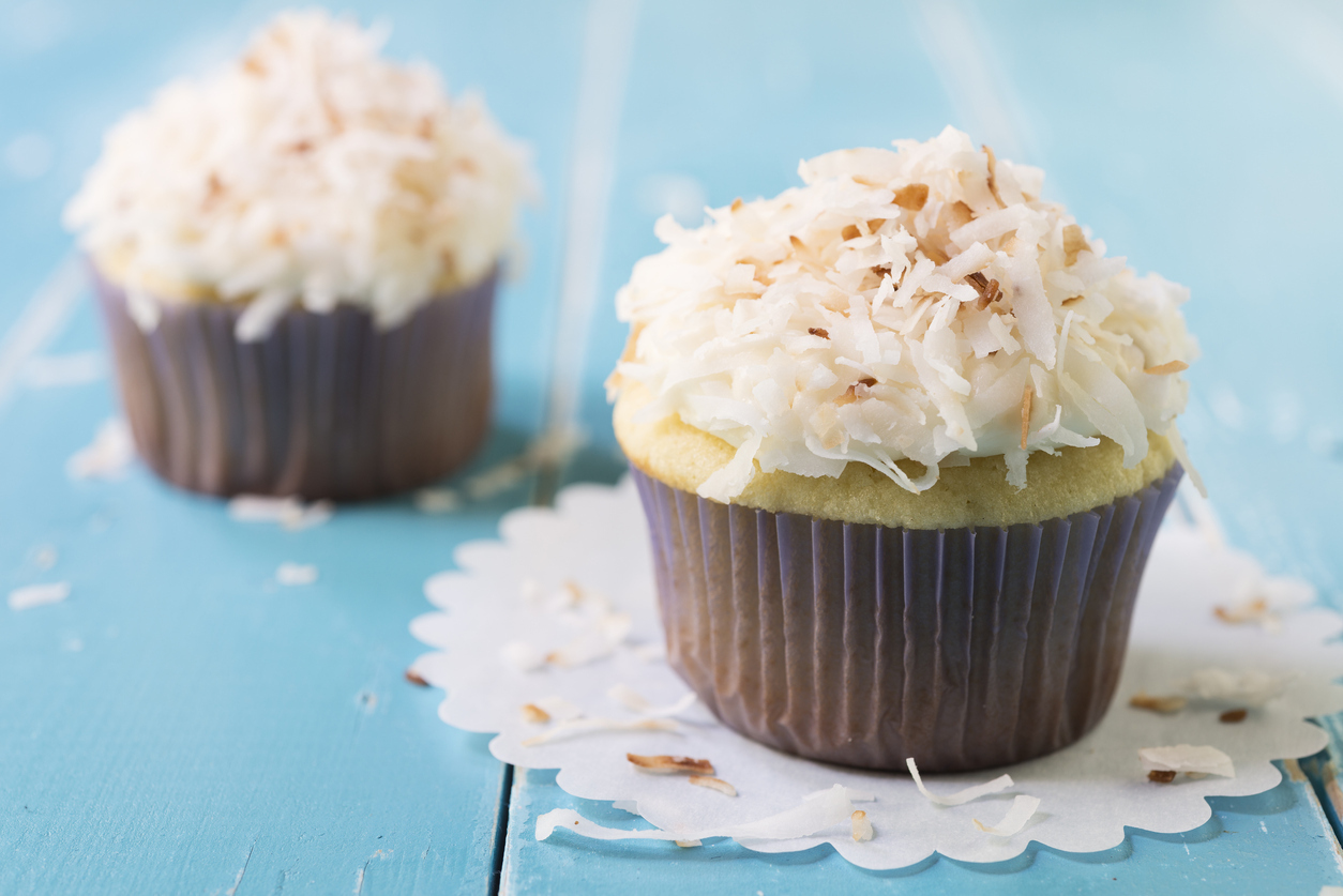 Two almond cupcakes with toasted coconut topping on a blue table.