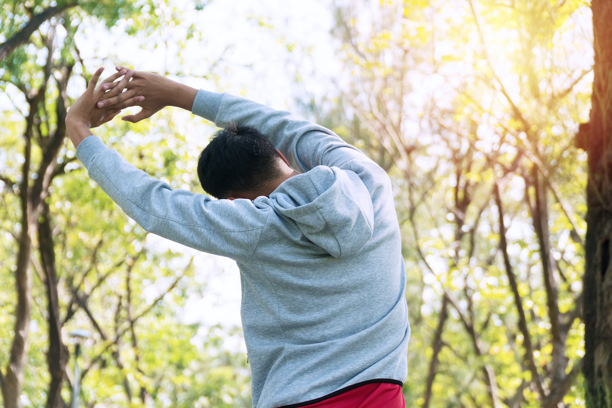 Back of athlete young man stretching arm shoulder before workout in the park. Trainer male warming up preparation body before running at outdoor. Healthy lifestyle concept.