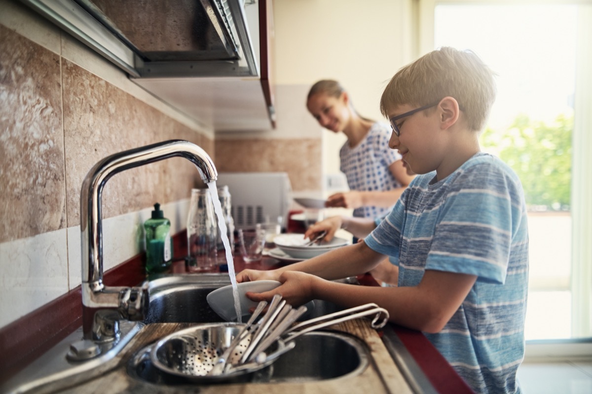 Three kids washing up dishes in kitchen. The boys and a girl are working together to help their parents.