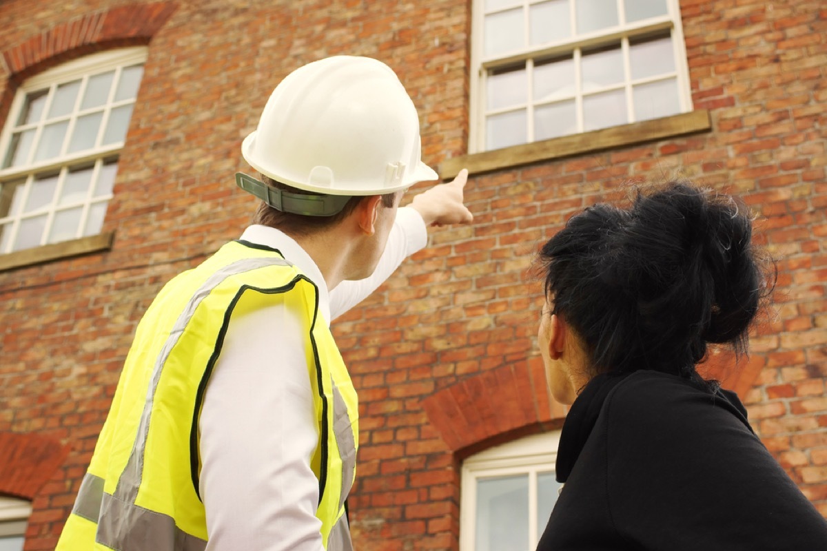 man in hardhat pointing to home's exterior window, signs your house is falling apart