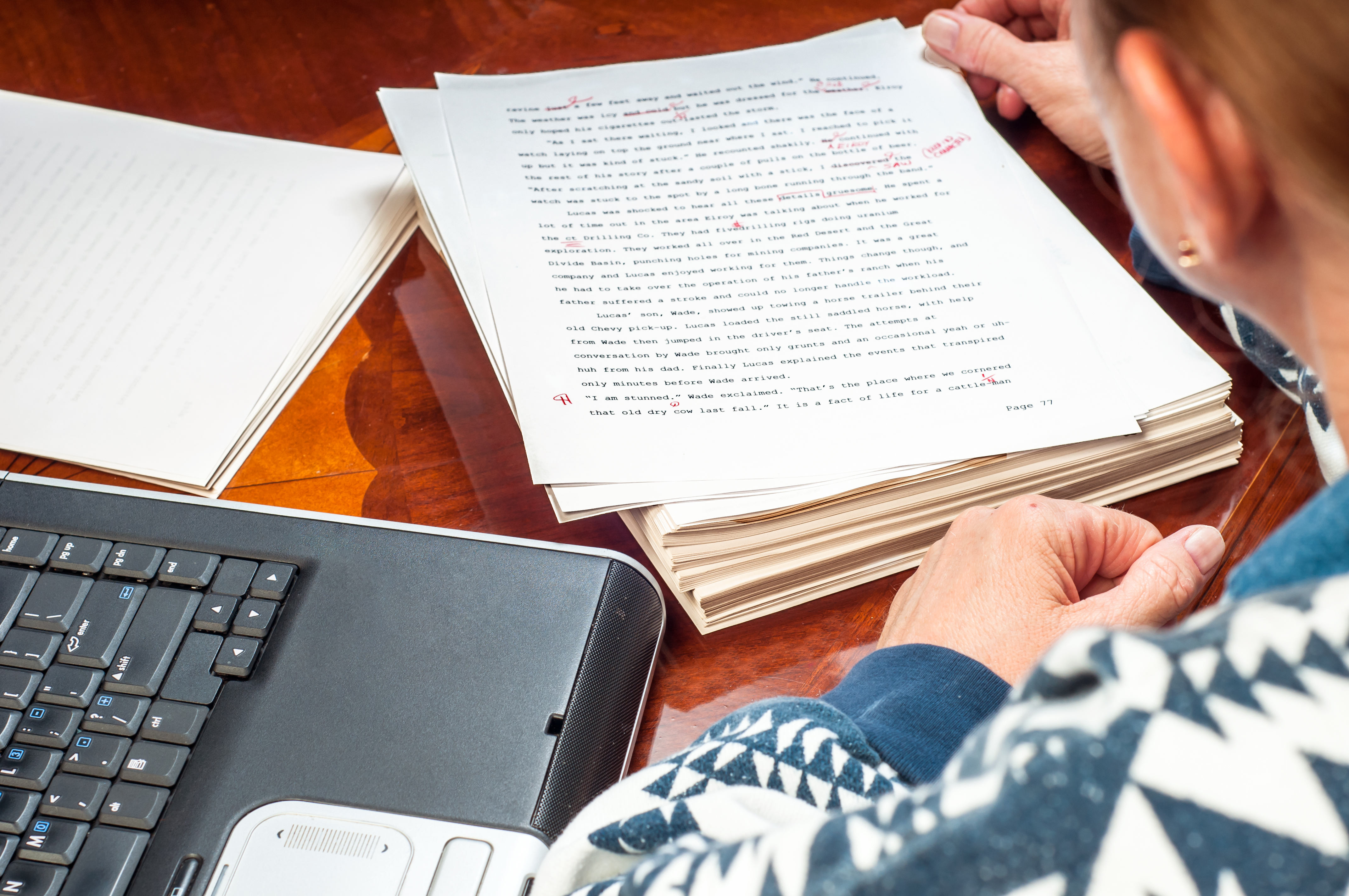 woman with stack of papers and laptop editing her novel