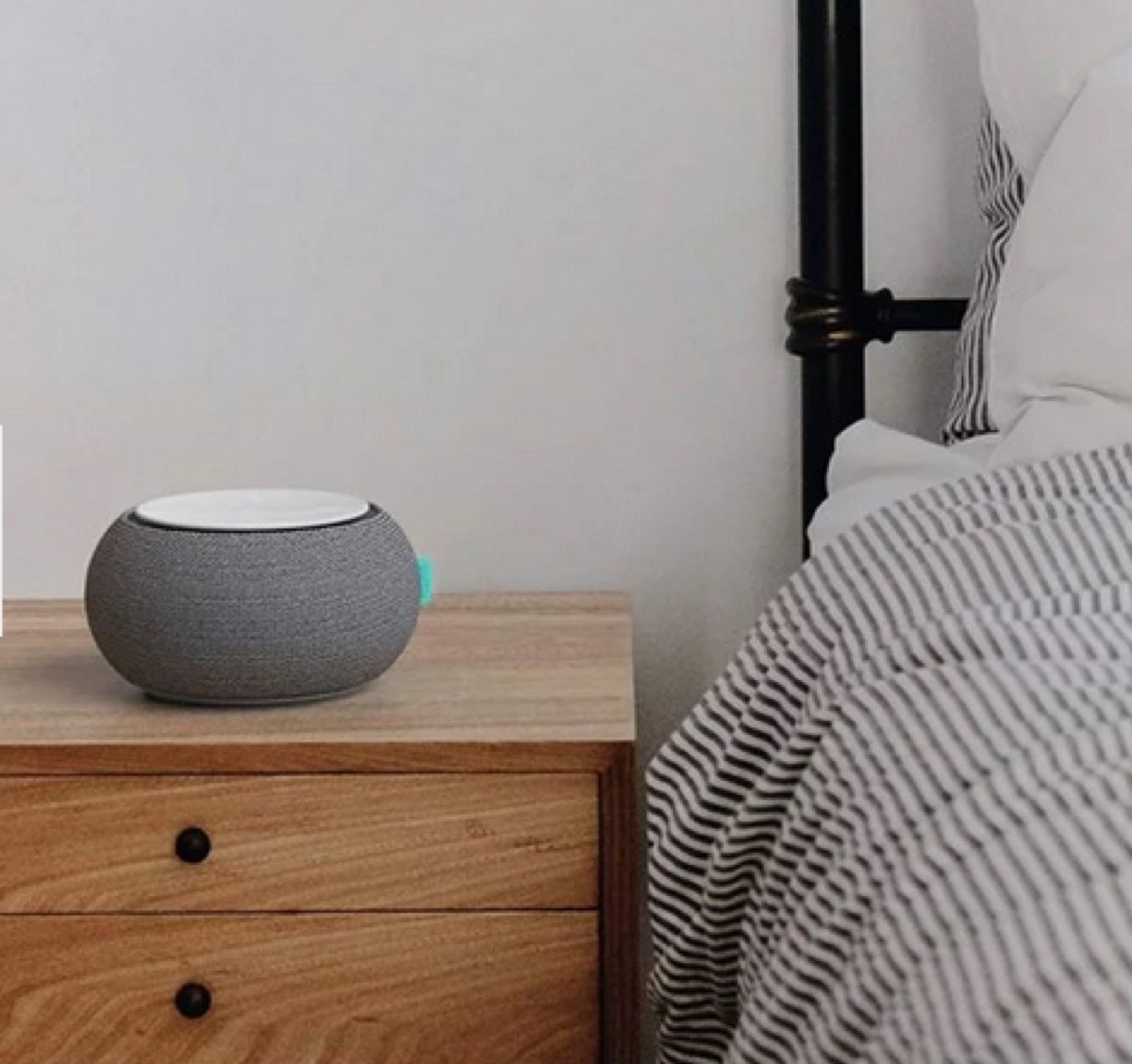 gray white noise machine on wooden nightstand next to bed with seersucker comforter