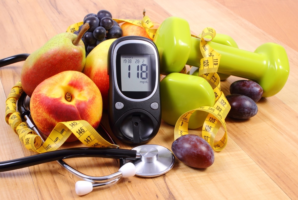 Glucose meter with medical stethoscope, fruits and dumbbells for using in fitness, concept of diabetes, healthy lifestyles and nutrition