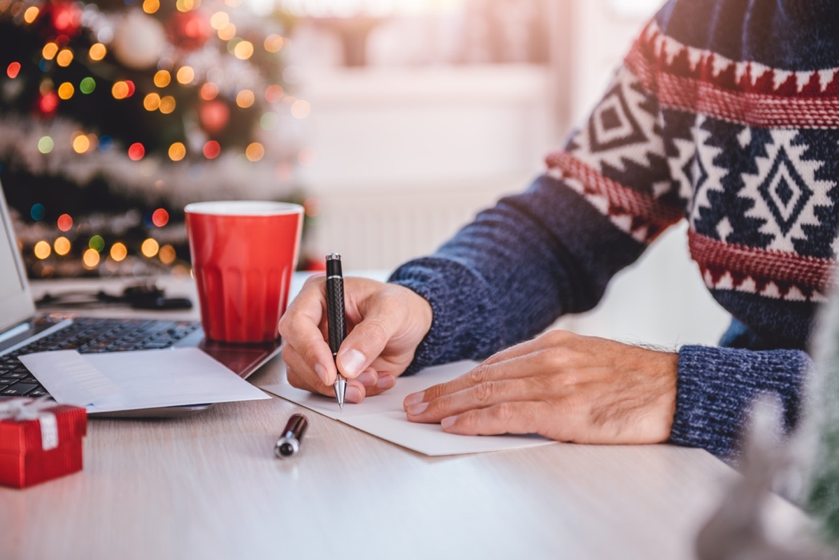 man writing holiday cards and funny 'out of office' messages in front of his laptop before the holiday break