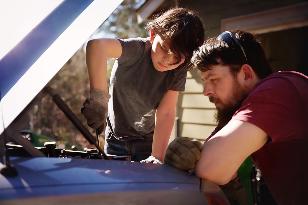 father teaching his son how to work on the motor of a car