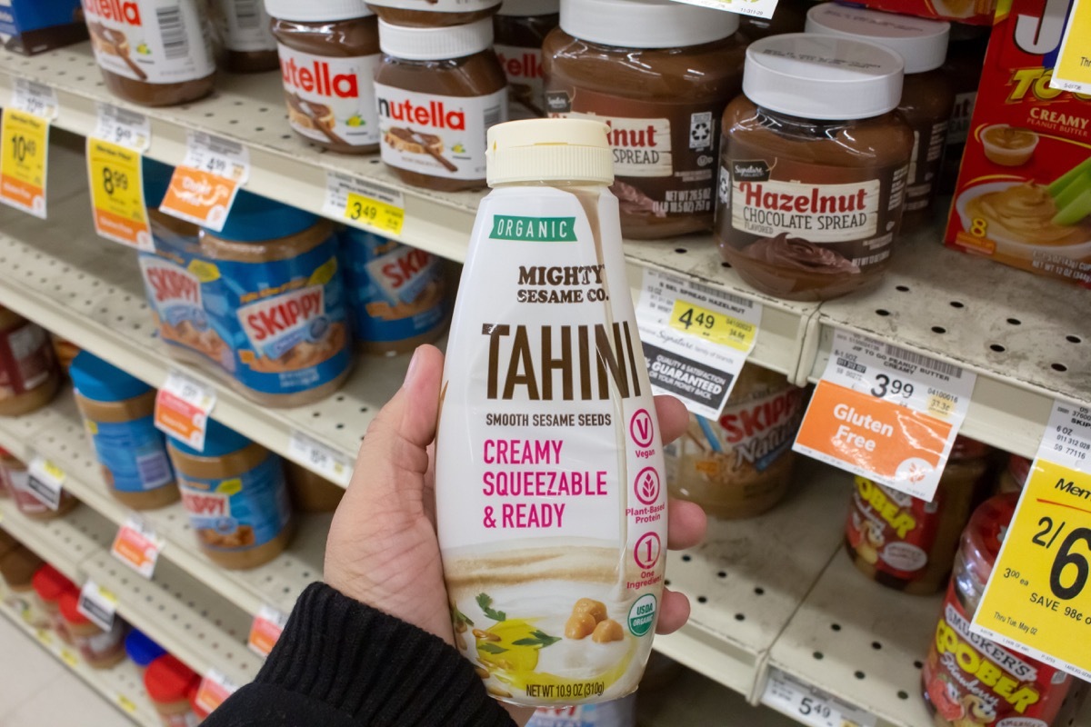 A view of a hand holding a bottled of Mighty Sesame Co. tahini, on display at a local grocery store.