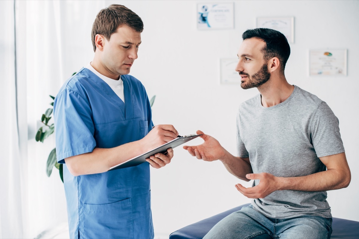 Patient sitting on couch and doctor writing prescription in massage cabinet at clinic