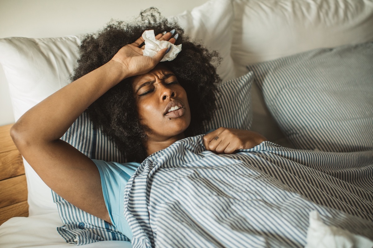 woman feeling sick at home. Lying in bed, drinking tea and medicine. Daytime.