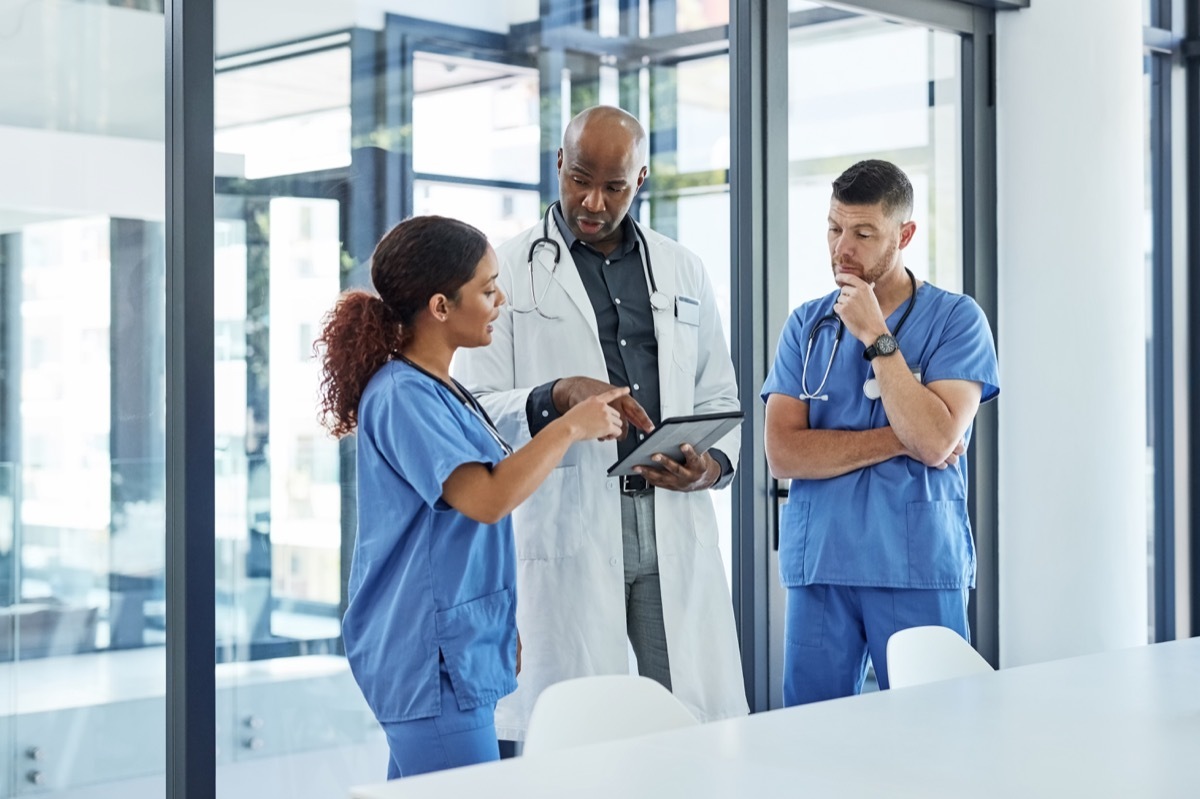 group of medical practitioners talking to each other while looking at a tablet