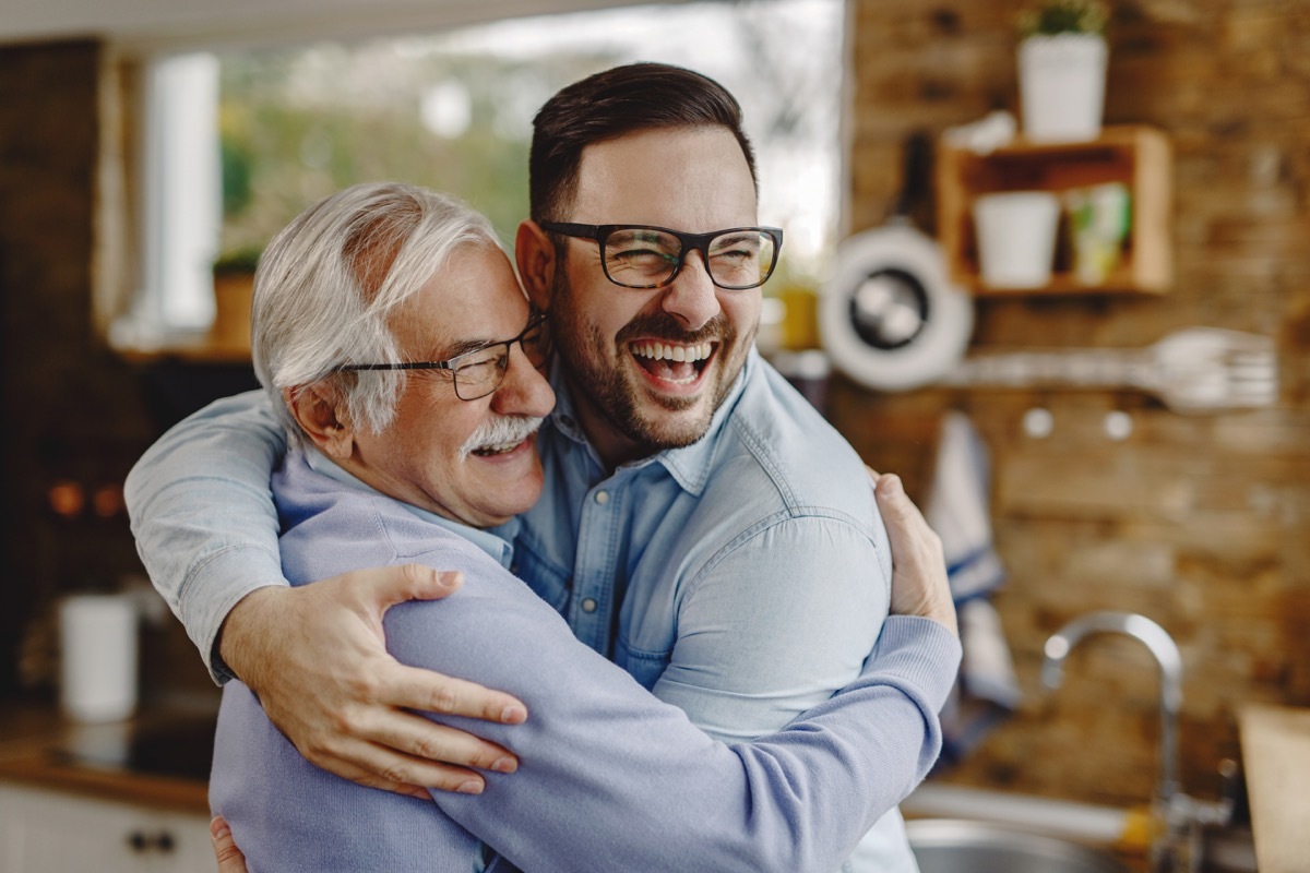 Happy mature man having fun while embracing with his adult son who came to visit him.