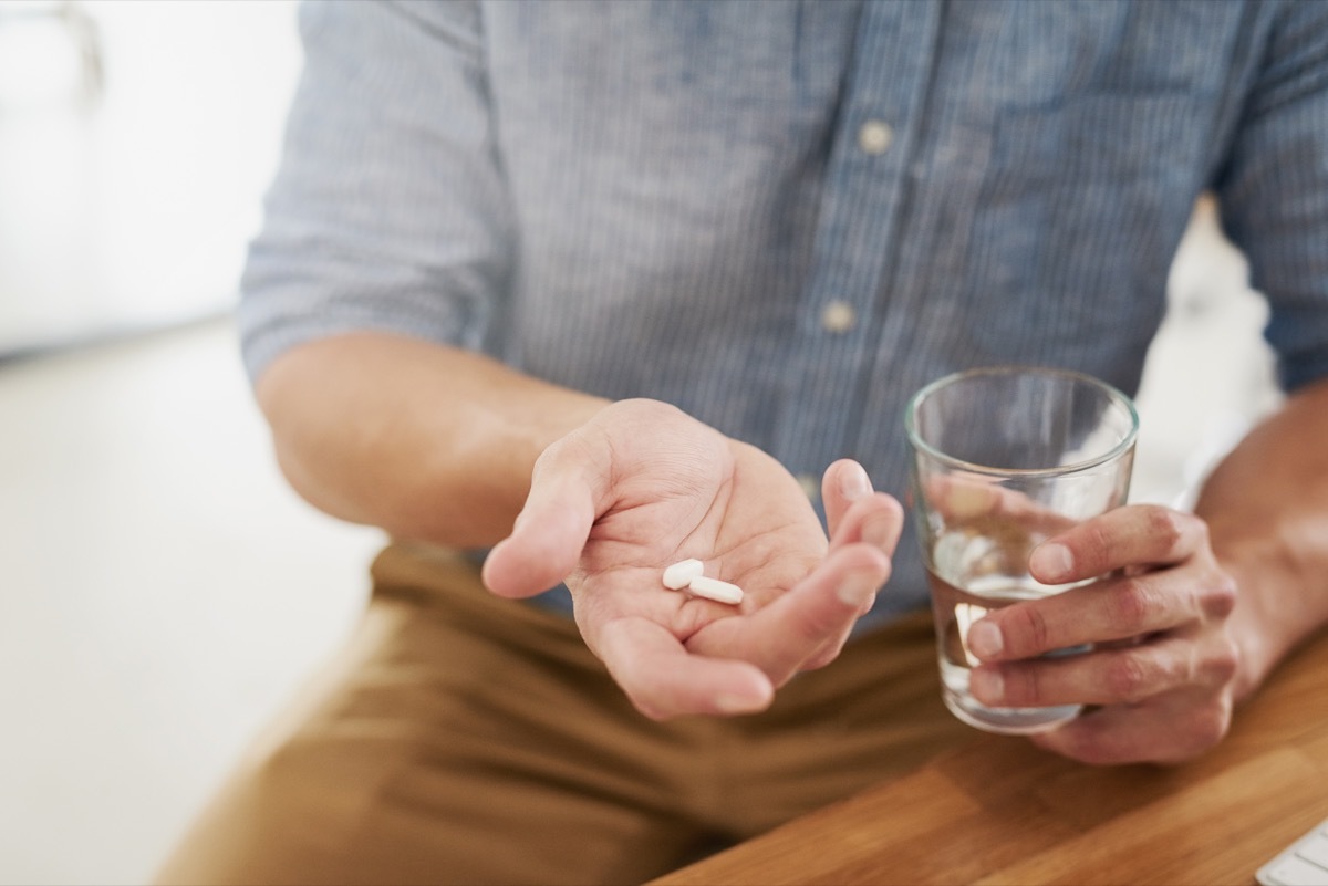 Closeup shot of an unrecognisable man holding a glass of water and medication in his hands