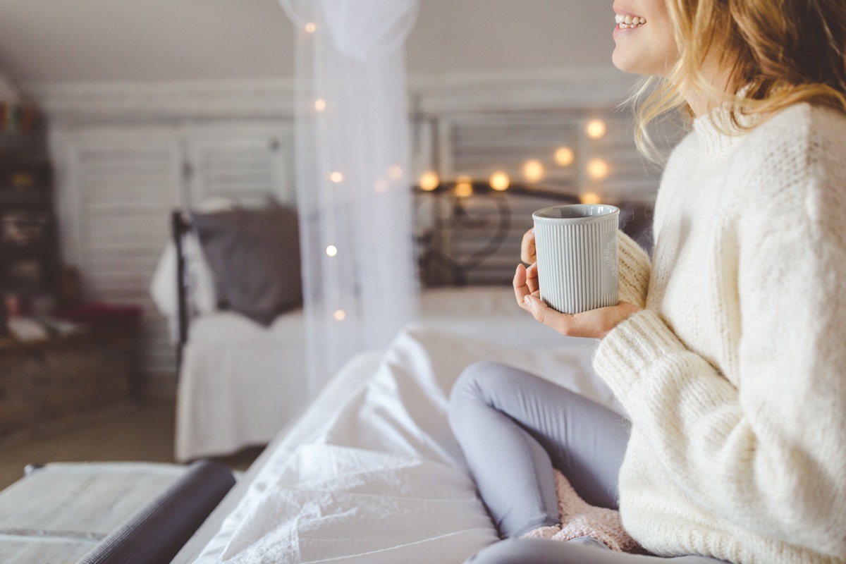 woman wearing white while sitting on her bed drinking a cup of coffee