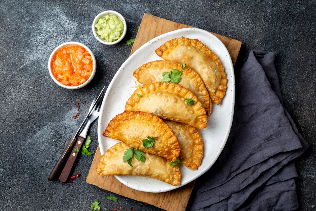 empanadas on white plate next to small plastic containers of salsa and guacamole