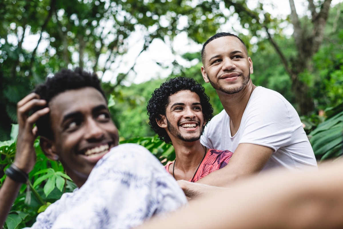 two young black men embracing with another black man in the forefront