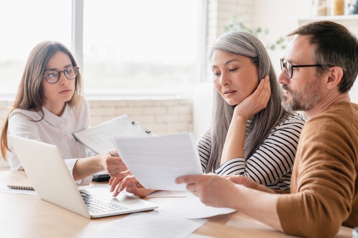 Young woman working with couple at desk with paperwork and laptop