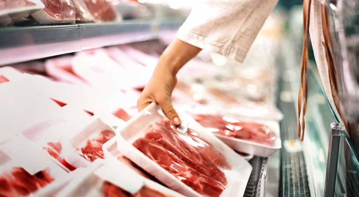 Closeup side view of unrecognizable woman chossing some fresh meat at local supermarket. The meat is cut into chops and packed into one pound packages. She has reached for a package of beef sirloin steaks.