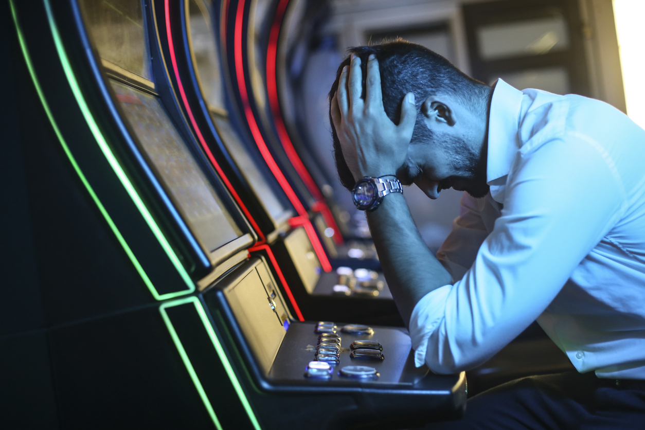 A young man sitting at a slot machine with his head in his hands