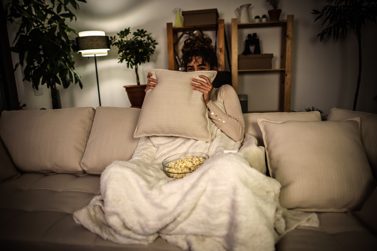 Photo of a scared woman watching a horror movie at night and eating popcorn