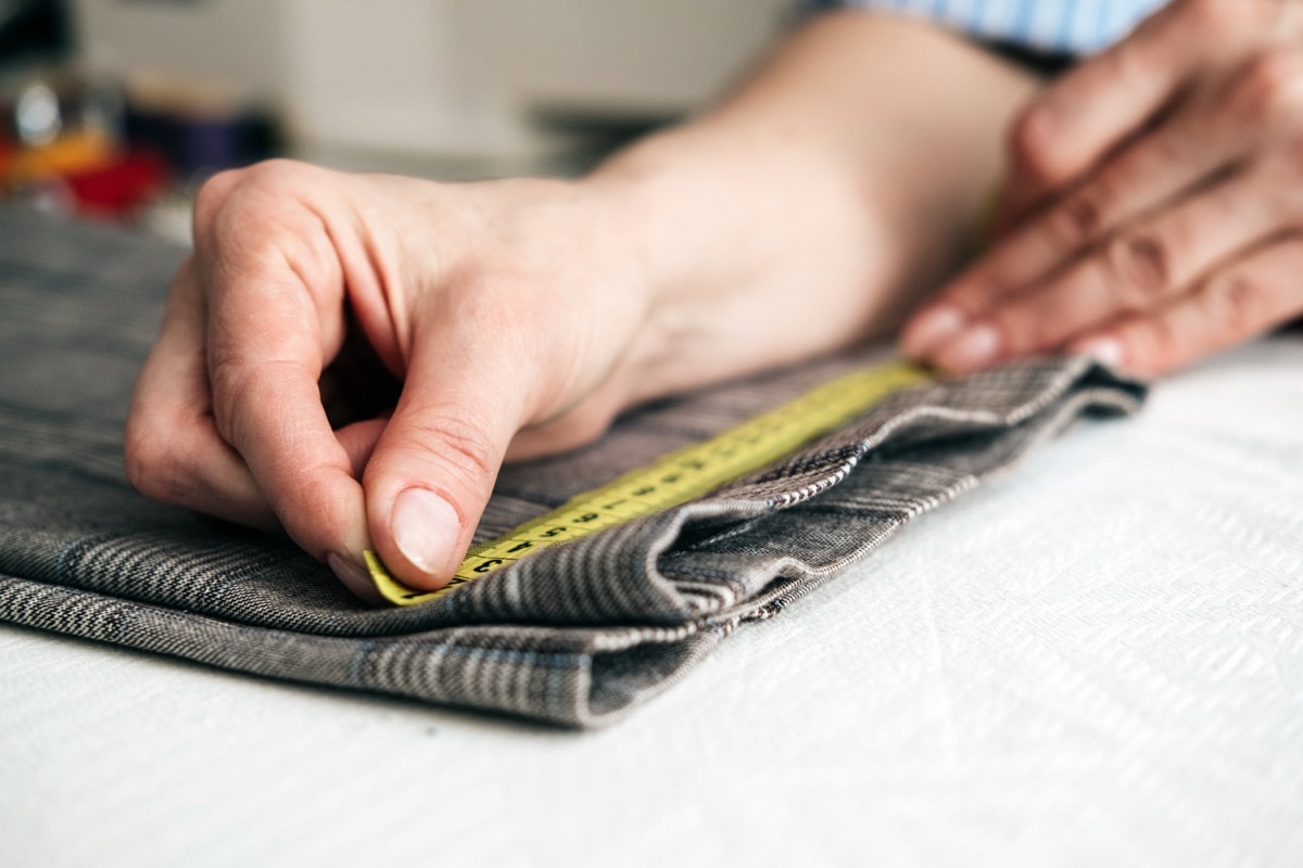 tailor using a measure tape to measure width of pants