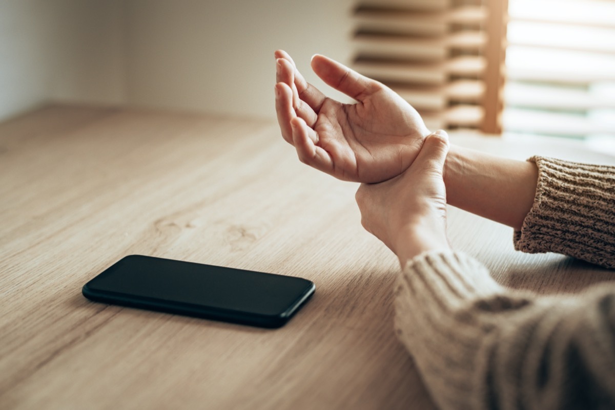 Woman holding her wrist pain from overuse smartphone.