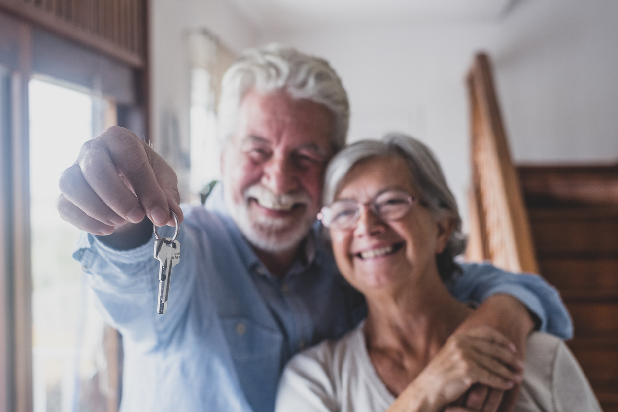 A senior couple hugging while holding keys to a new home