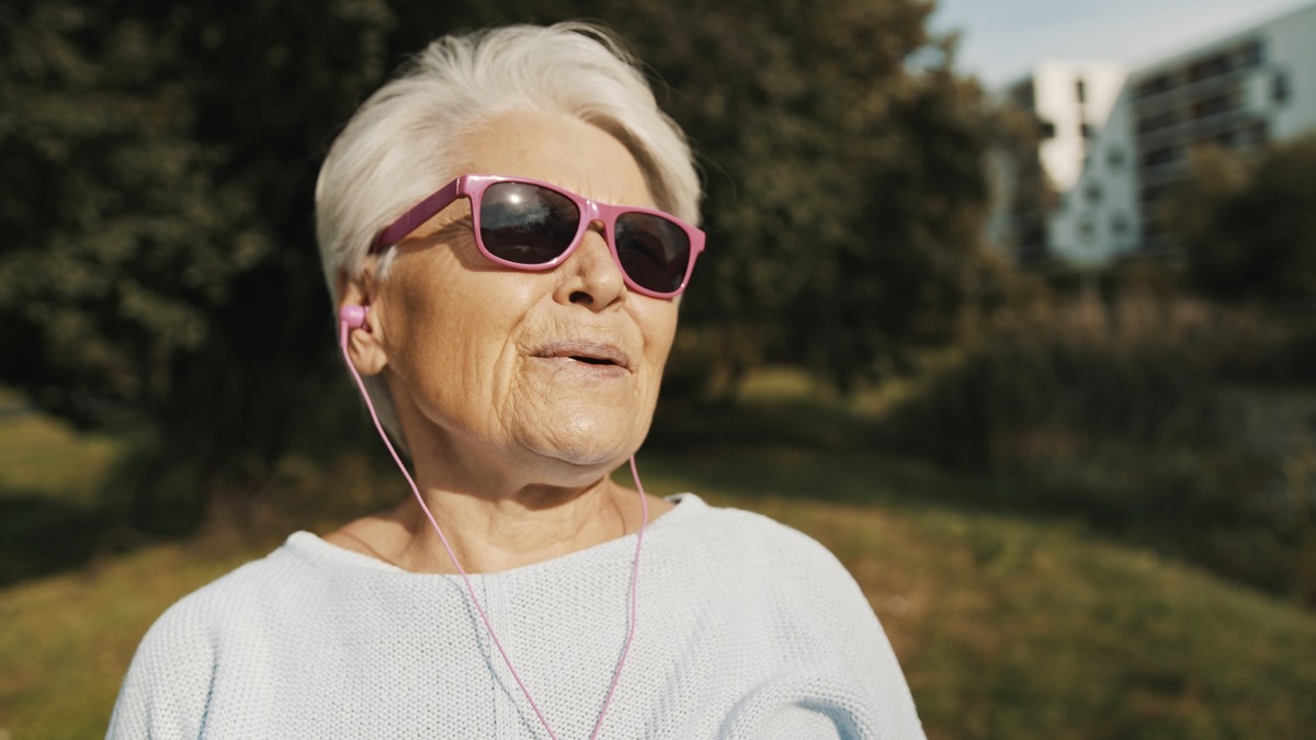 Cool grandmother with pink sunglasses and headphones listening music.