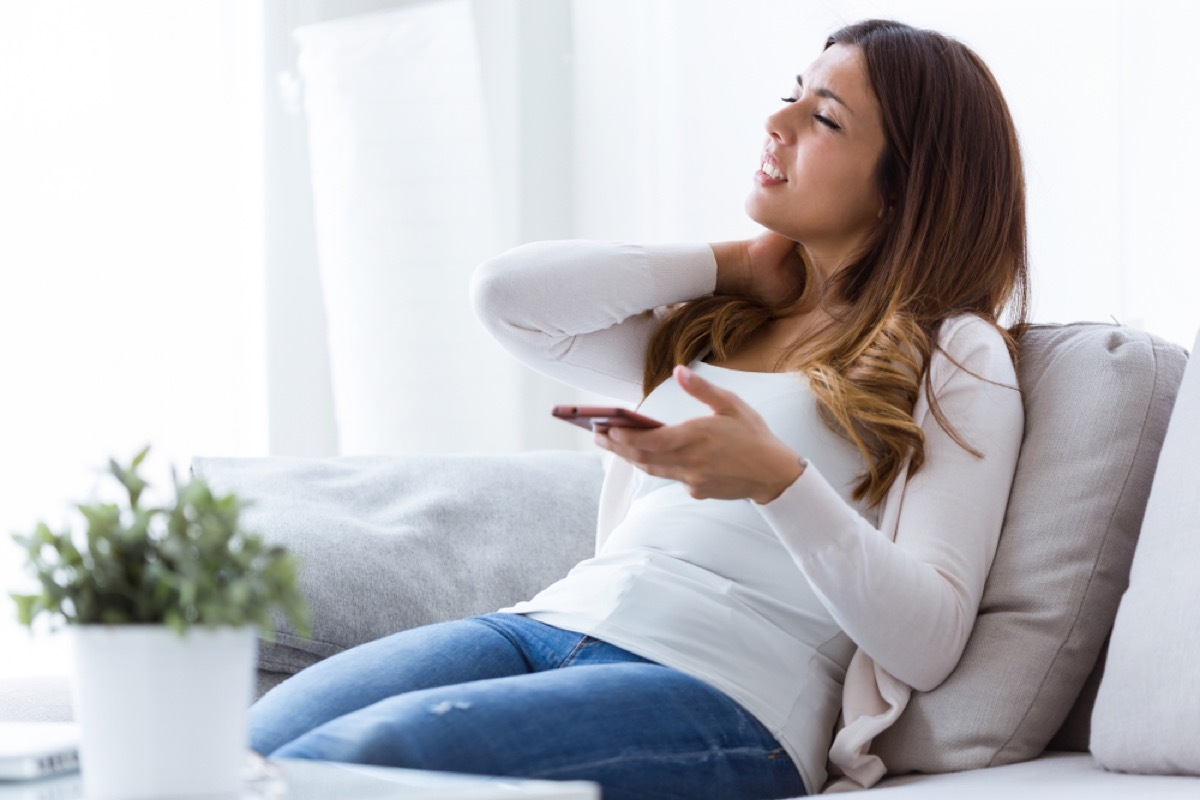 tired young woman with neck pain holding her mobile phone at home