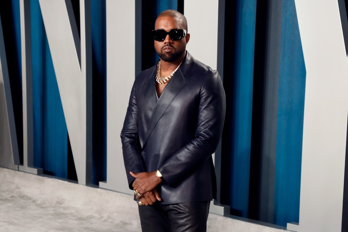 kanye west wearing a leather suit in front of vanity fair sign