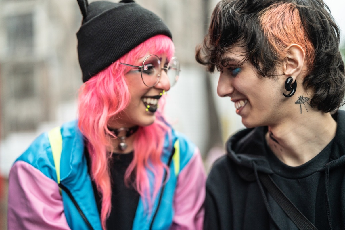 young white woman with pink hair smiling at young white man with piercings