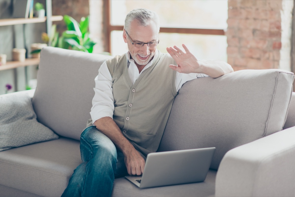 Cheerful excited joyful intelligent clever glad relaxed grandpa using netbook telling relatives friends