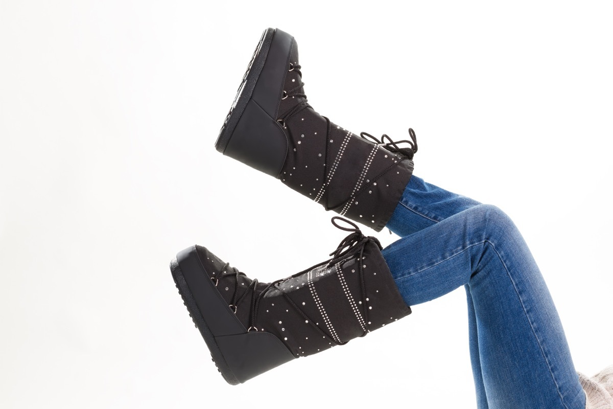 Fun black winter moon boots. Legs of girl in jeans and moon boots on white background. - Image