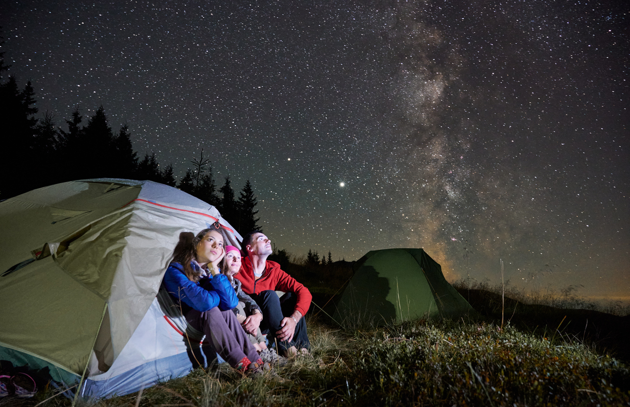 A family camping in a tent while looking up at the Milky Way and night sky