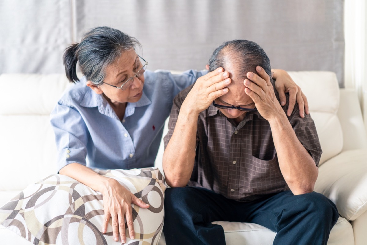 older asian woman comforting older asian man on couch