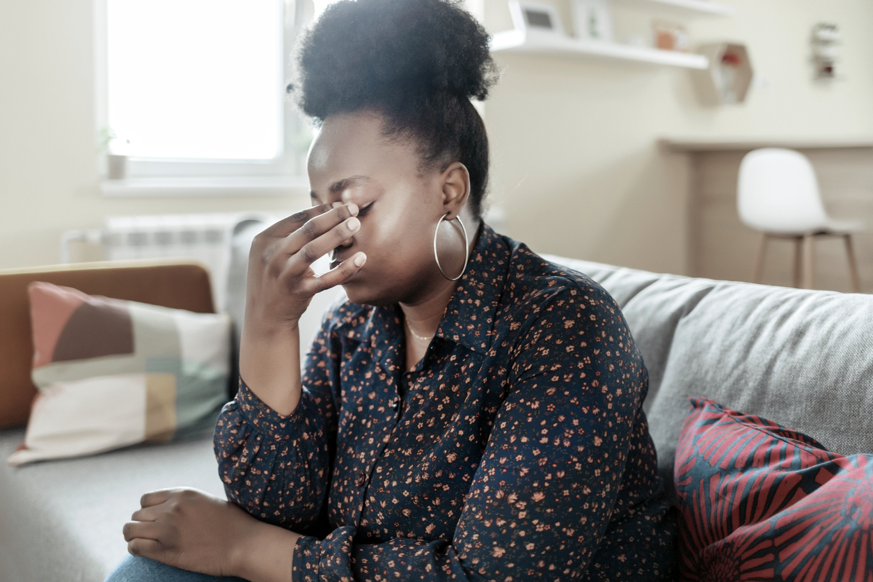 Young African American Woman Sitting on a Couch, Holding Her Head, Having a Strong Headache