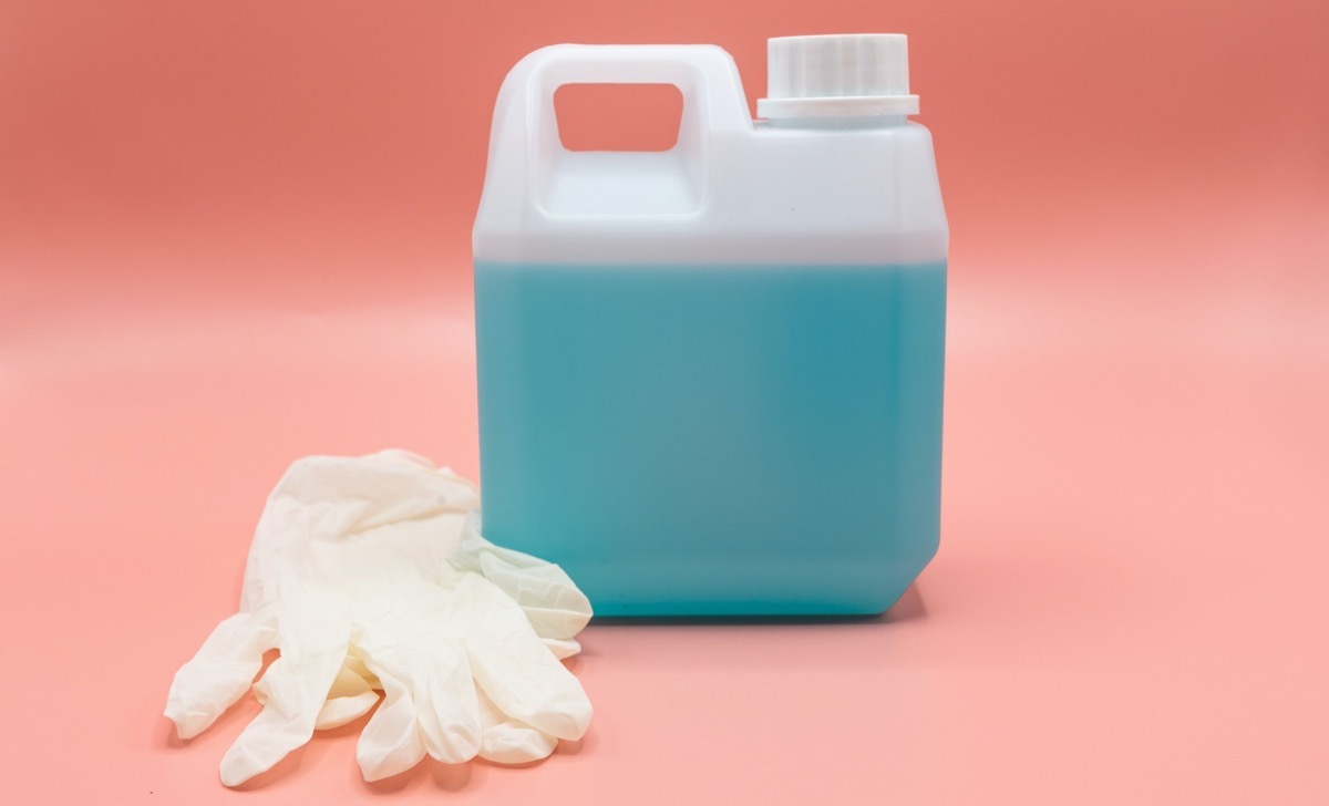 Human hand in rubber elastic glove with sanitizer bottle on yellow background. Concept of coronavirus protection, COVID-19 pandemic, global quarantine. 