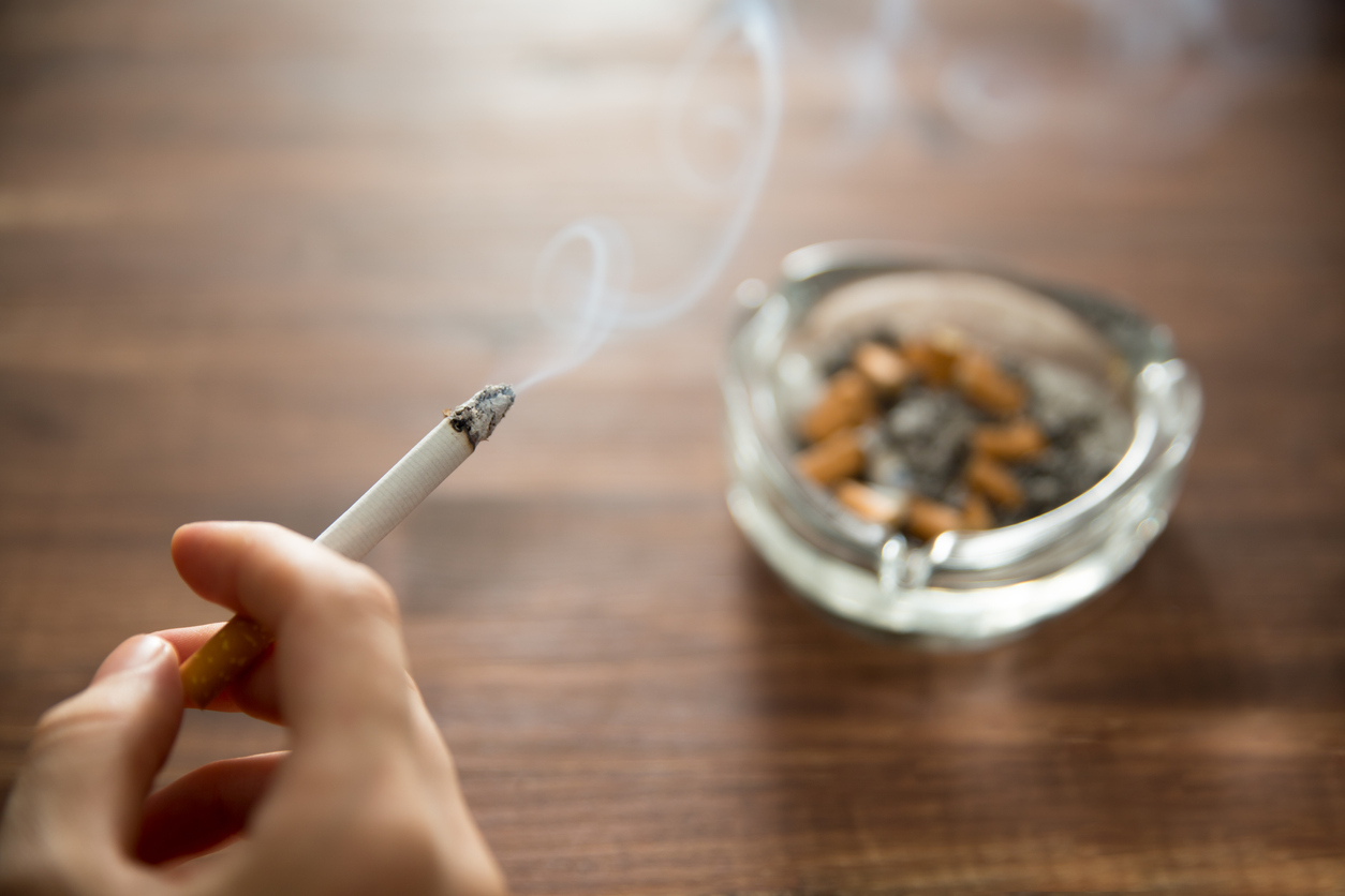 Person holding burning cigarette in hand with ashtray.