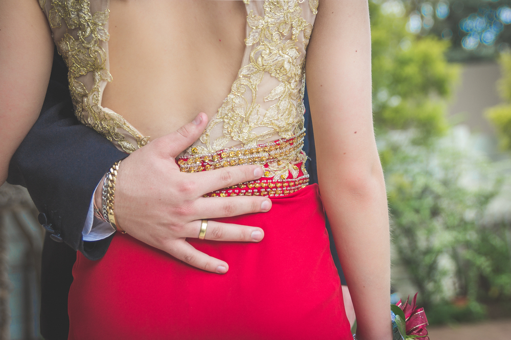 Man holding woman around waist with his hand on woman's lower back dressed in formal wear