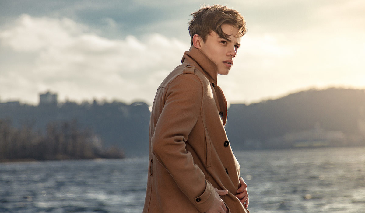 blond haired boy wearing a camel overcoat