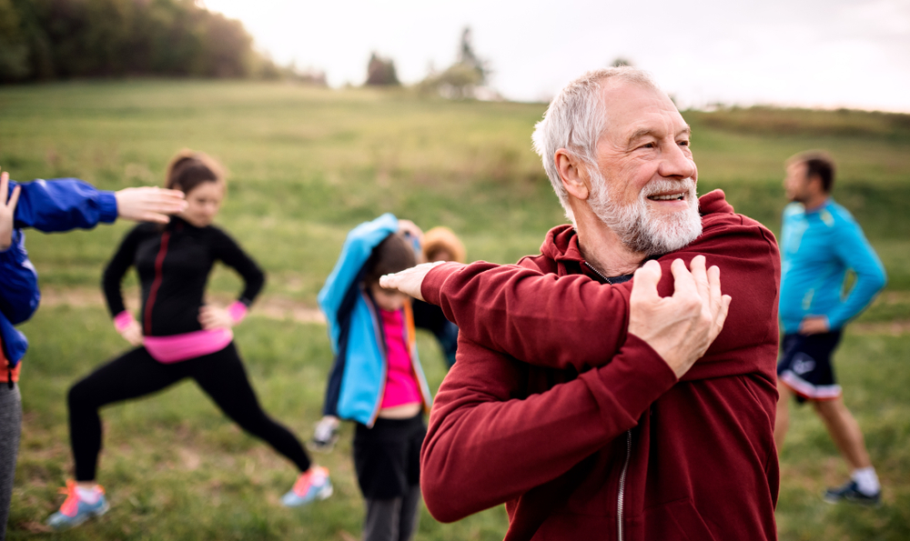 A senior man stretching with a group of people in a park while exercising