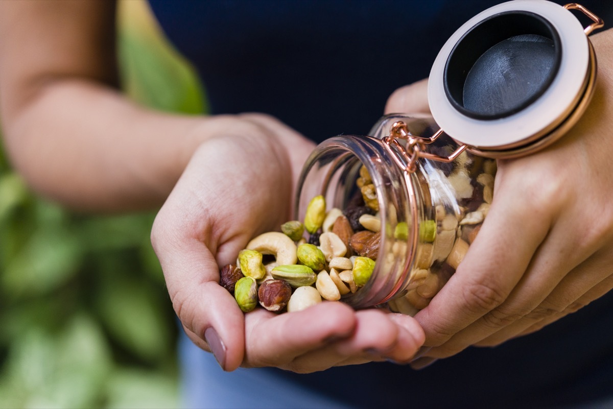 Brunette model hand holding glass hermetic pot with mix of nuts.