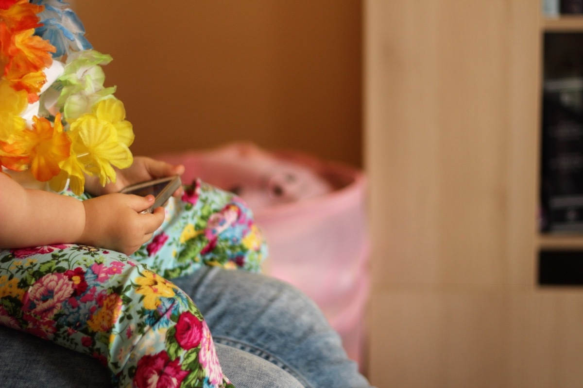 child wearing a Hawaiian shirt and leis holding a smart phone