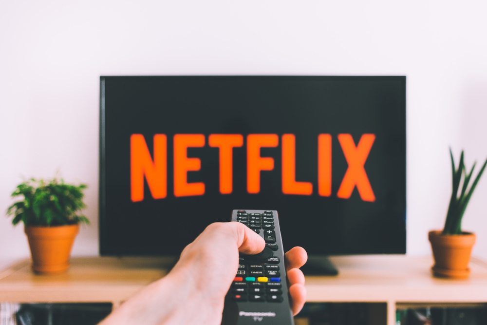 A person pointing a remote control at a TV with the Netflix logo on it