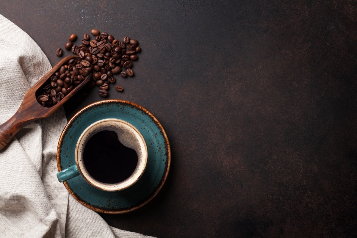 Cup of coffee on a blue saucer next to coffee beans and scooper